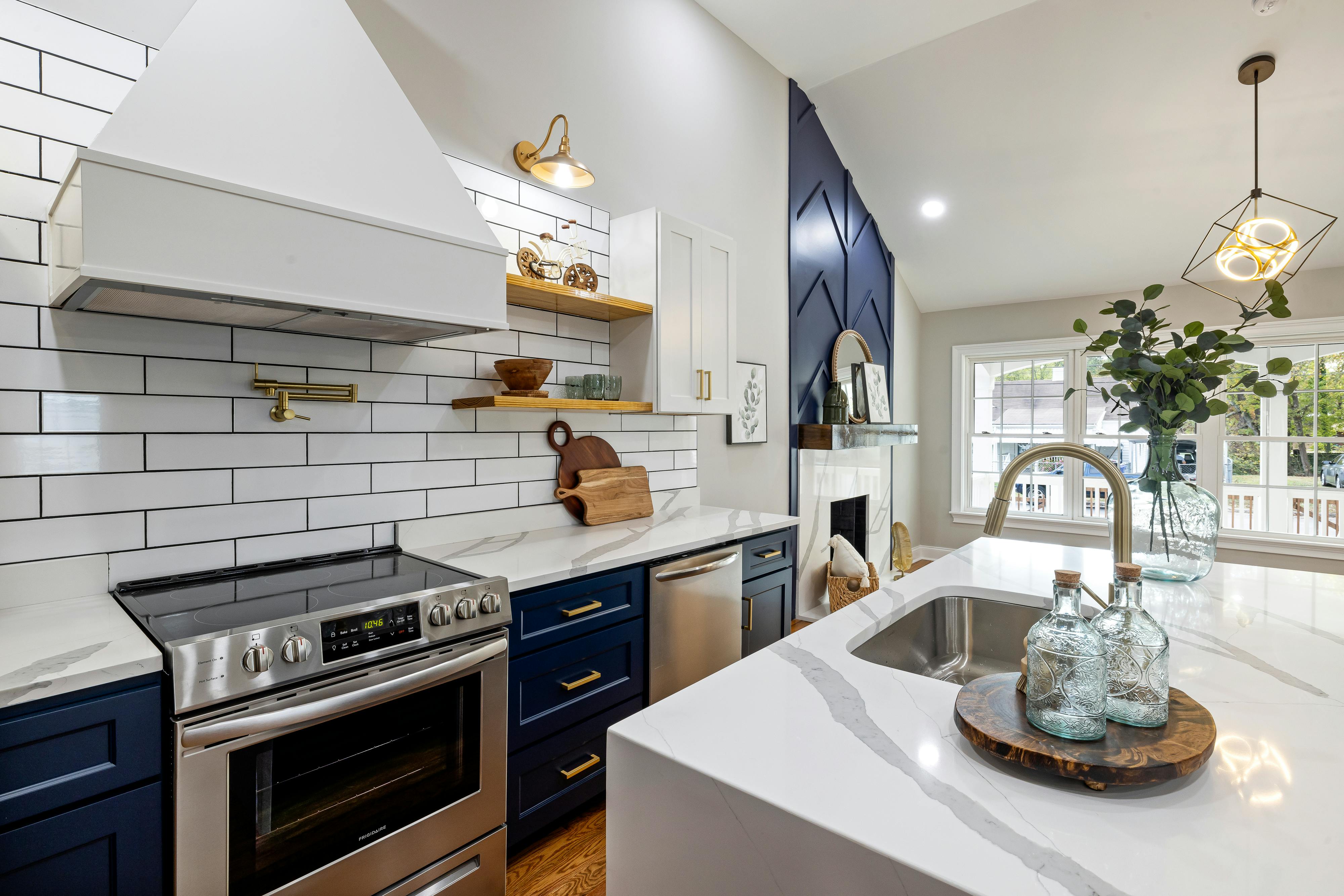 Contemporary kitchen with navy blue cabinets, white marble countertops, subway tile backsplash, and brass lighting